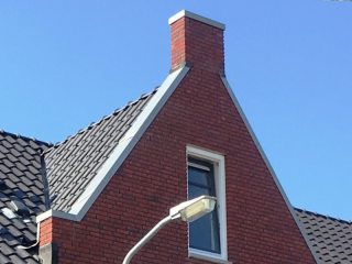 Prefab kopschoorsteen met rode steenstrips op de kopgevel van een woning met pannendak.